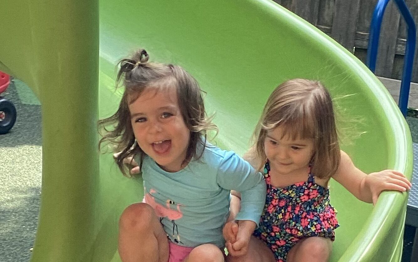 Two toddler girls sliding down green slide