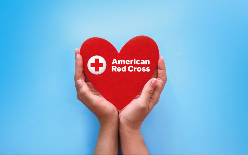 Two hands holding a red felt hewart with American Red Cross logo