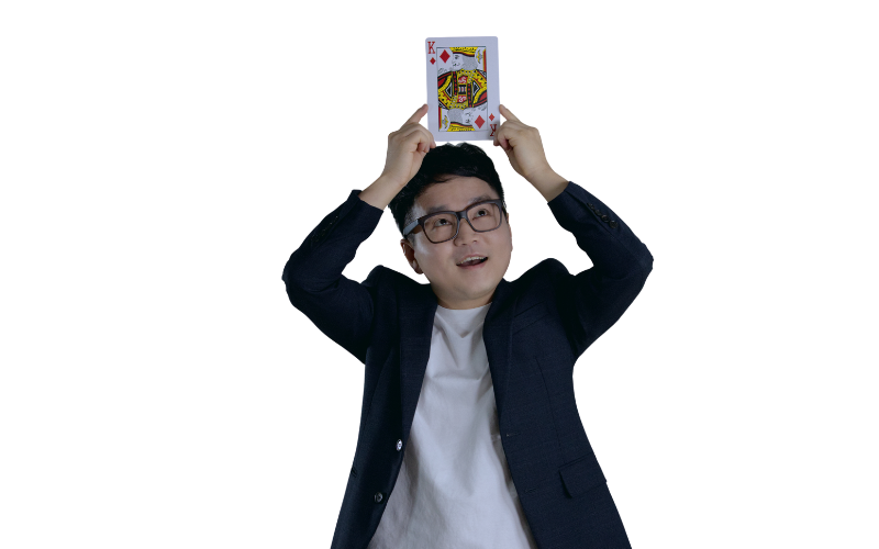 Jeki Yoo holding an oversized playing card over his head while looking up towards it.