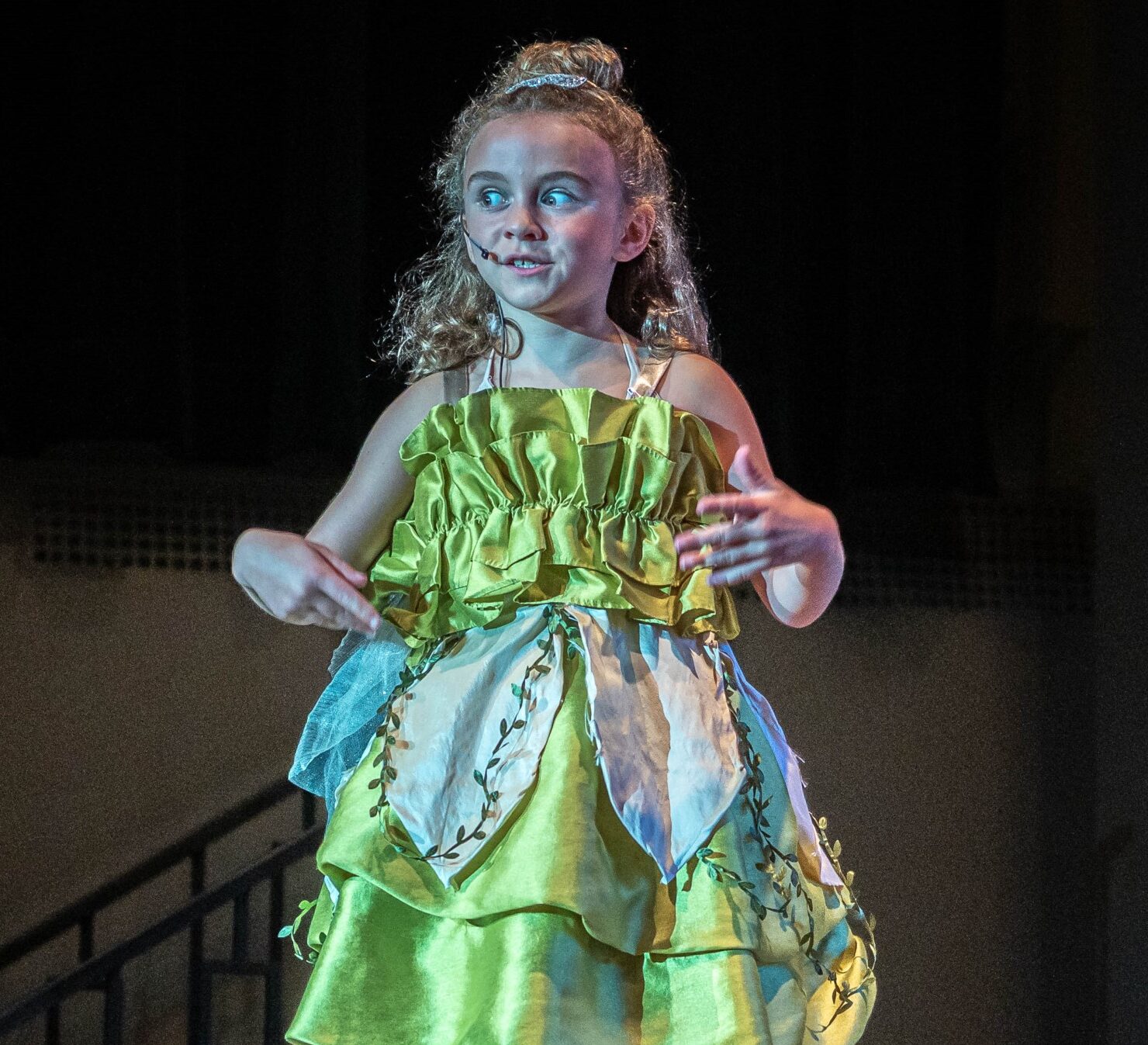 Young girl with curly blonde hair in a green dress playing Tinkerbell in a Peter Pan theatre performance