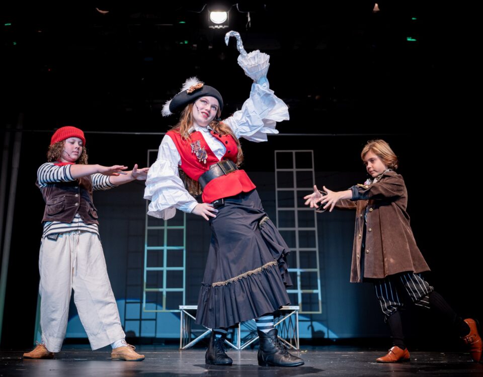 Girl in a pirate costume dancing with two other castmates dressed as pirates at a Peter Pan theatre performance