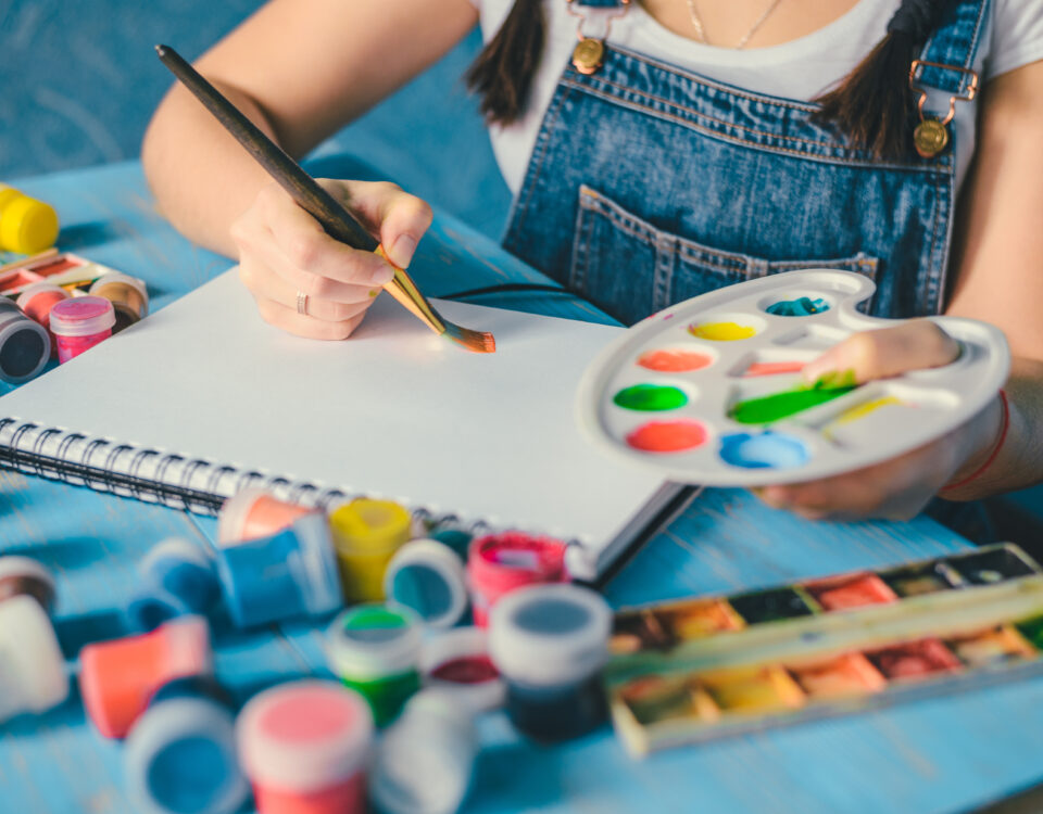 Pretty smiling young woman drawing a picture with poster paint