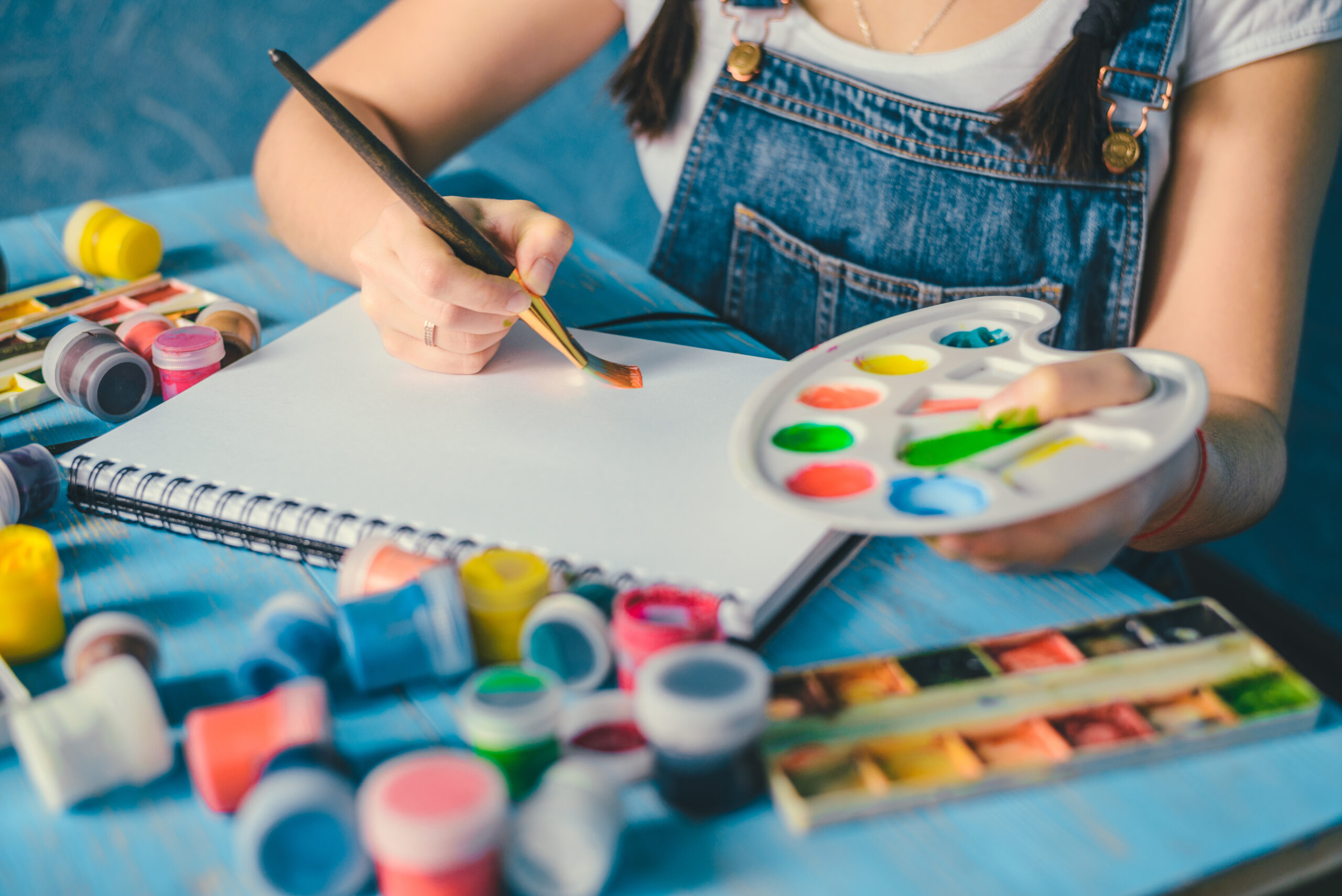 Pretty smiling young woman drawing a picture with poster paint