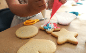 Plain sugar cookies sitting on a table with small hands squeezing frosting onto them. 