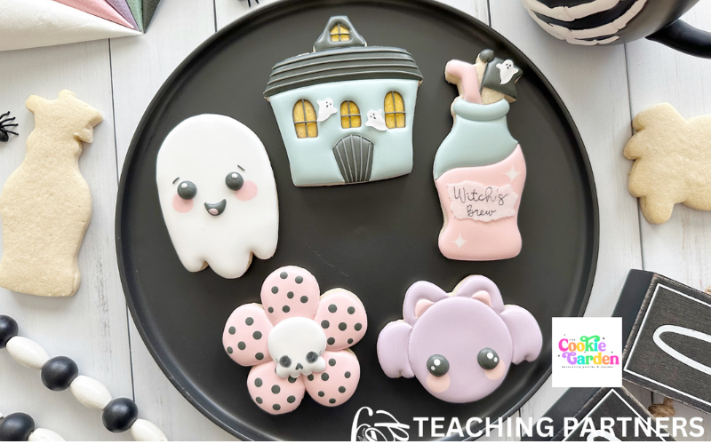 5 sugar cookies on a black plate decorated in a cute Halloween theme: a ghost, a haunted house, a bottle of witch's brew, a bat and a flower with a skull in the middle