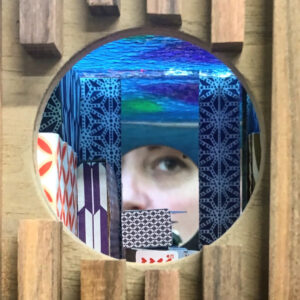 A photo of the inside of a sculpture that has a womens face that is partially obstructed by pieces of paper that have different patterns on them. Above her head is blue glass that gives the illusion she is underwater