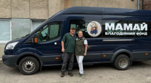 Megan Carroll Himmer and Alan Himmer standind in front of a sprinter van in Ukraine. The van has a logo and text written in Ukrainian. 