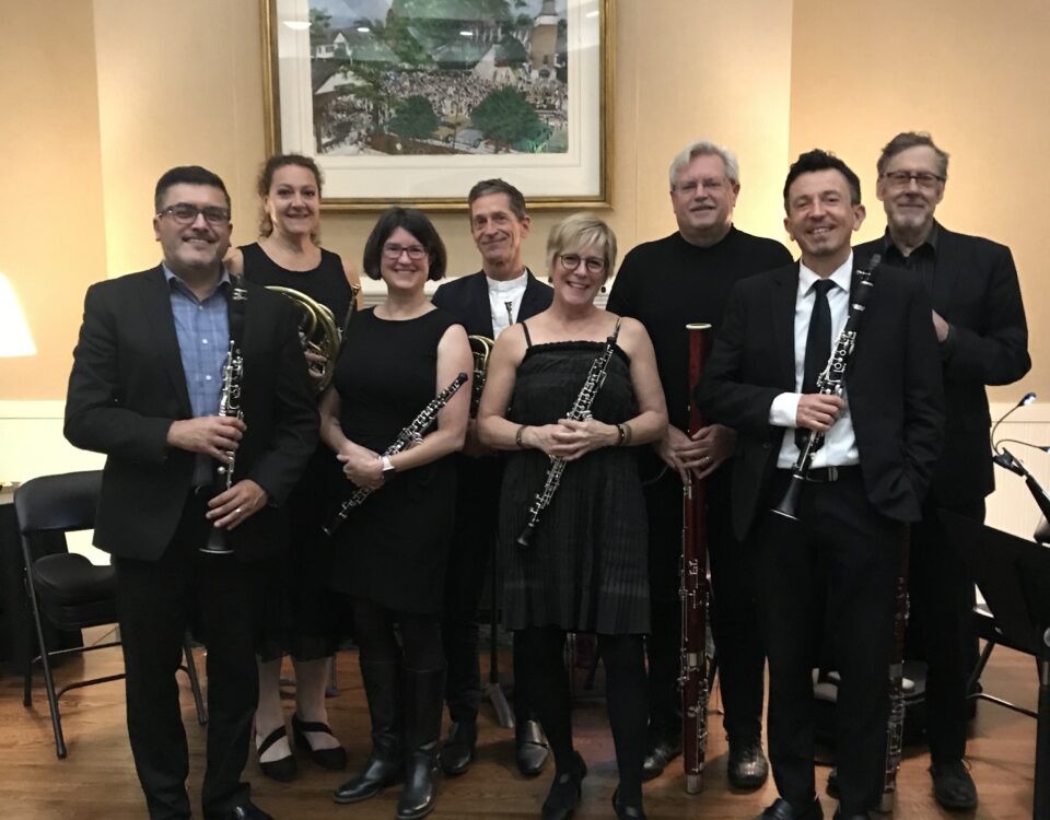 Members of the Woodwind celebration octet gathered in front of the mantel in the Stuart Community Room holding their instruments and looking at the camera