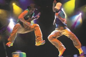 Buckets n' boards members on stage mid jump while holding guitars