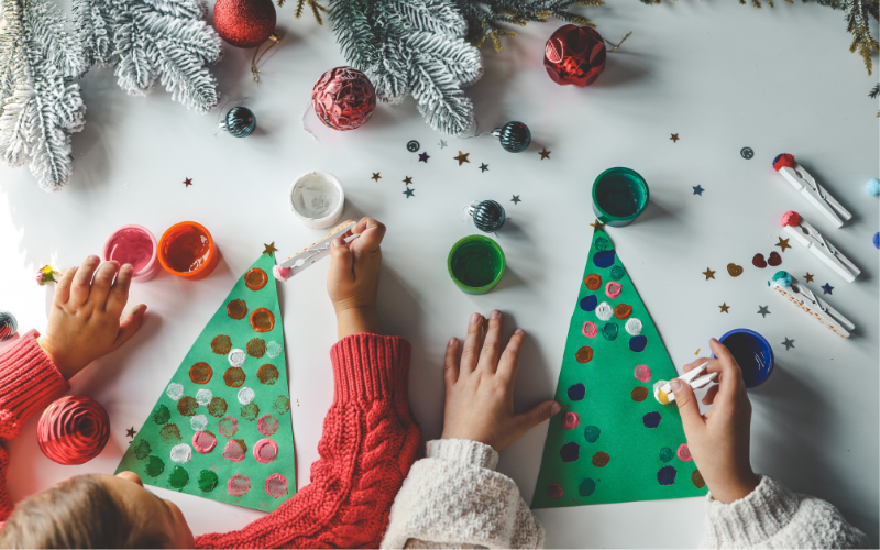 Two children using homemade stamps to colorfully decorate a green paper Christmas Tree.