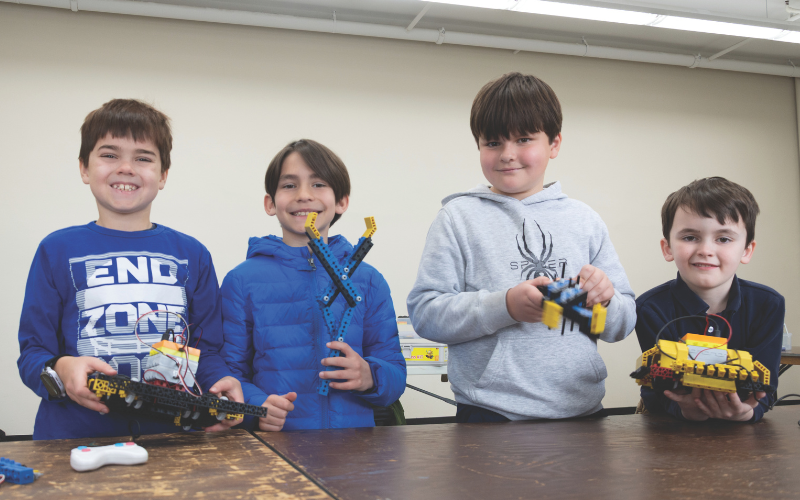 Four boys stans in a row at a table proudly show off their Robothink camp: Robopetz constructions.