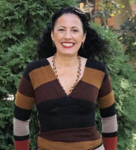 Gorton Hospitality Coordinator Jasmin Rodriguez is standing in front of foliage and smiling directly at the camera.