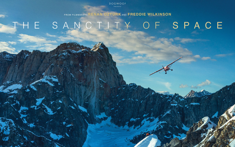 Poster for the film 'The Sanctity of Space'- the image is of snow covered mountains with a propeller plane flying overhead and two mountain climbers reaching a peak below the plane.