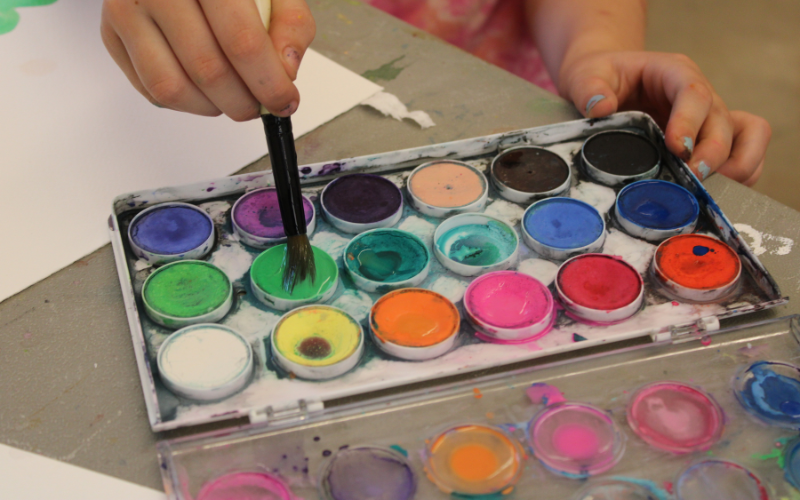 Watercolor palette with child dipping a brush into the green paint