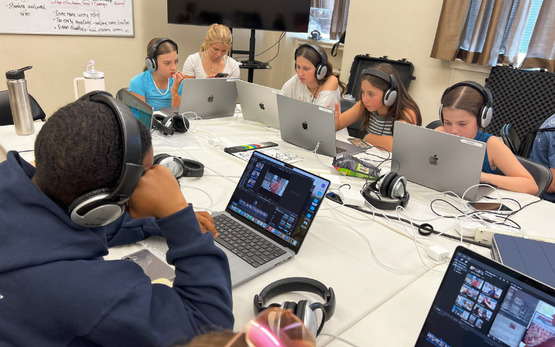 A group of middle school students sitting around a table with computers at new media film camp