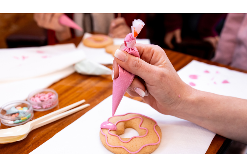 Woman decorating a circular cookie with pink icing in the Cookie Decorating: Ladies Night class
