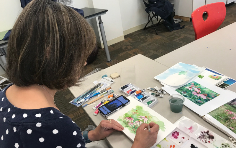 the back of a womans head while she paints with watercolor