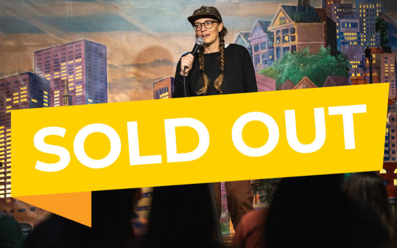 An image of Emily Catalano performing on stage with a yellow Sold Out banner over it