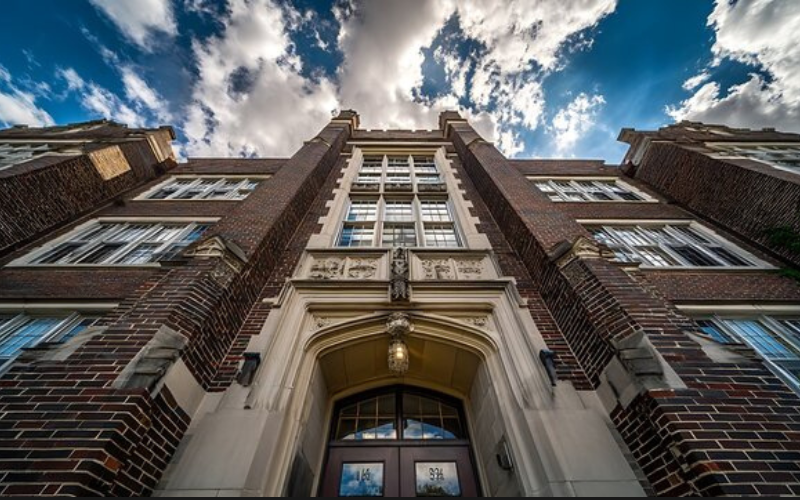 A photo of a brick, victorian style school building. The camera is positioned in front of the school entrance and is pointed up to show the height of the building,