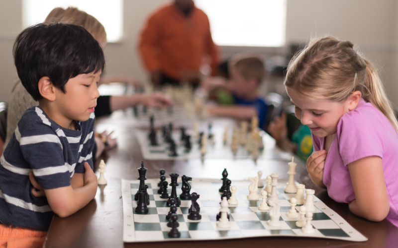 Young girl and boy sit at table and learn to play chess