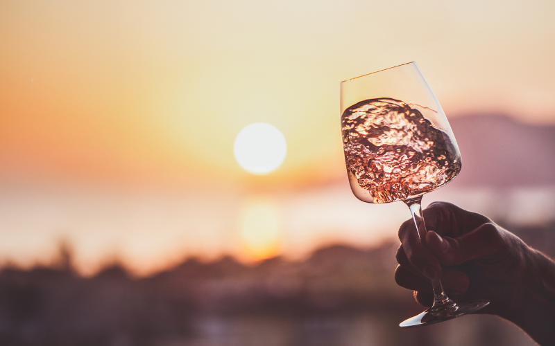 hand holding wine glass nd swirling wine with sunset in the background, summer wine tasting