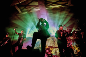 LowDown Brass Band are performing onstage. They are backlit by green and purple lights and are all dressed in black,