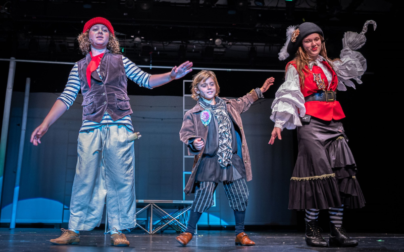 An image of 3 kids dressed as pirates and dancing on stage. The pirate to the far right has a hook on her hand.