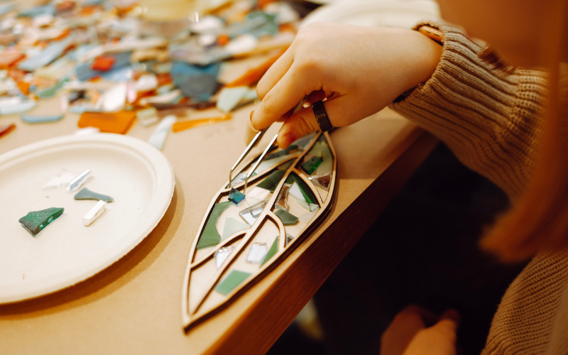 Woman holding tweezer and placing pieces of glass to make Botanical Mosiac