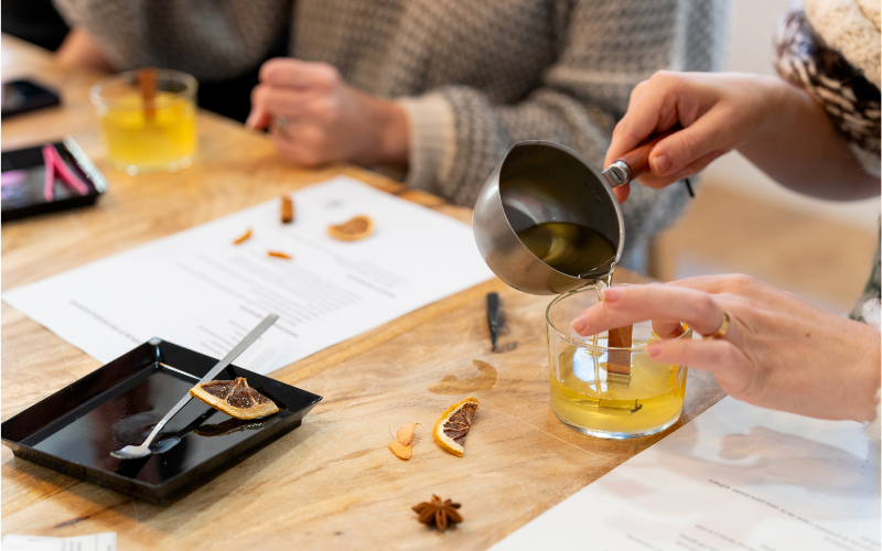 Candle Making, person pouring liquid wax into a glass conatiner with a wooden wick
