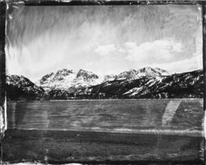 A black and white tin type photo by Max Li. There are mountains in the distance and a lake in front of it with a cloudy sky