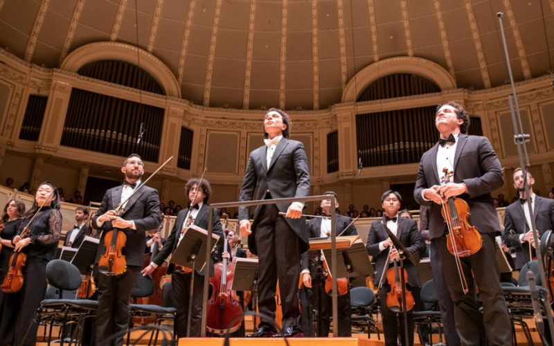 The members of the Avant symphony orchestra are standing onstage facing the audience.