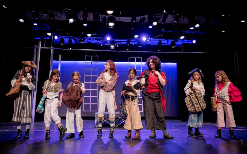A group of children perform on stage in develop musical theater skills class